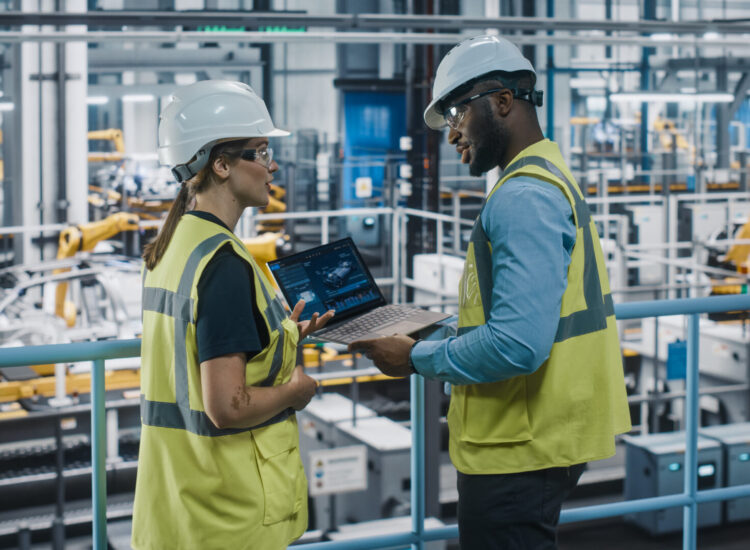 Male Specialist and Female Car Factory Engineer in High Visibility Vests Using Laptop Computer. Automotive Industrial Manufacturing Facility Working on Vehicle Production. Diversity on Assembly Plant.